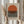 May include: Person in beige outfit holding framed minimalist poster featuring orange semicircle above black horizontal lines on cream background, with dried pampas grass stems visible to the left, set against white curtained window backdrop in soft natural lighting.