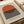 May include: Framed Bauhaus-inspired poster print featuring a large orange semicircle above horizontal black and white stripes on cream background, displayed on neutral bedding next to a curved ceramic vase in soft natural lighting