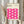 May include: Hands holding a framed poster with pink wavy geometric pattern against cream background. Frame appears light wood with clean lines. Dried pampas grass visible on left side. Person wearing beige ruffled sleeve top. Soft natural lighting creates shadows on neutral wall behind.