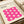 May include: A framed Bauhaus-style poster with bright pink wavy geometric pattern on cream background, displayed on white shelving next to rolled papers and neutral decor. The minimalist print features repeating curved shapes creating an optical wave effect, with black text identifying the German design school and dates 1919-1933.