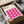 May include: Hands in white gloves carefully unpacking a framed Bauhaus poster from cardboard box with tissue paper. The cream-colored poster features bold pink wavy geometric shapes in a repeating pattern. Black frame sits in brown shipping box on white surface with tape dispenser visible in background.