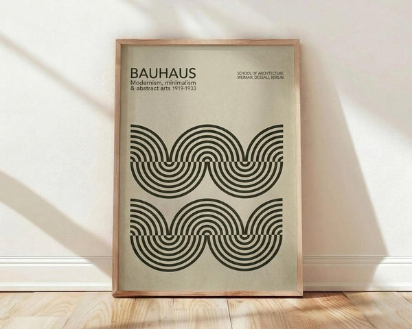 May include: Framed Bauhaus-inspired poster with beige background featuring black concentric semicircles arranged in repeating wave pattern. Modern minimalist design in light wood frame, leaning against white wall on light wooden floor with soft natural lighting and shadows.