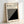 May include: Framed minimalist black and white geometric poster leaning against white wall on light wooden floor. Design features diagonal black stripes creating angular pattern against cream background, with "BAUHAUS" and "Modernism, minimalism & abstract arts 1919-1933" text at top. Natural wood frame casts soft shadows in bright lighting.