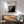 May include: Bauhaus modernist poster with black and white diagonal striped geometric design in wooden frame, hanging above mid-century modern walnut credenza with table lamp, next to sage green upholstered armchair with wooden arms in bright sunlit room with white walls and hardwood floors.