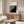 May include: Black and white Bauhaus poster with diagonal stripes in thin wooden frame, displayed above walnut credenza in minimalist living room with cream chair, glass coffee table, and modern lamp. Clean Scandinavian-style interior with neutral walls and natural lighting.