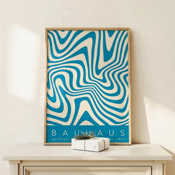 May include: Framed poster with flowing blue and cream swirled pattern in Bauhaus style, displayed on light wood dresser against white wall. Small white wrapped gift box sits in front of the wooden-framed artwork. The abstract design features organic curved lines creating a hypnotic wave-like effect in teal blue on cream background.