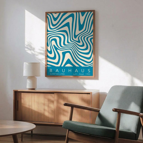 May include: Framed Bauhaus exhibition poster with turquoise and cream swirling geometric pattern displayed above mid-century modern wooden credenza. Scene features sage green upholstered armchair with wooden frame, white table lamp, and round coffee table. Warm natural lighting creates shadows on white wall in minimalist living room setting.