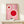 May include: Framed pink poster with geometric red circles and white lines in Bauhaus style, displayed on light wood console table next to small wrapped gift with twine and evergreen sprig against cream wall