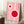 May include: Framed pink poster with geometric white circles containing red centers, displayed in modern room setting. Artwork features Bauhaus-style design with cream/white connecting elements on bright pink background. Wooden frame leans against white wall on textured cream rug, with coffee cup on wooden block nearby and beige fabric visible.