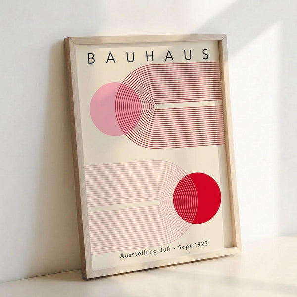 May include: Framed Bauhaus-style poster with geometric design featuring pink and red circles intersected by curved parallel lines on cream background. Modern minimalist art print in light wood frame, leaning against white wall. Clean contemporary aesthetic with vintage 1920s design influence.