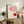 May include: Framed Bauhaus exhibition poster with geometric red and pink shapes and curved lines displayed on rustic wooden sideboard alongside fern plant, ceramic vase, and books in cozy living room setting with leather furniture and neutral wall