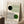 May include: Framed Bauhaus-style poster with geometric design featuring flowing curved lines in green and black, with black and green circles. The minimalist artwork displays "BAUHAUS" at top and "Ausstellung Juli - Sept 1923" at bottom on cream background. Light wood frame leans against white wall corner next to wooden stool with white coffee cup and saucer, positioned on textured cream rug in bright natural lighting.