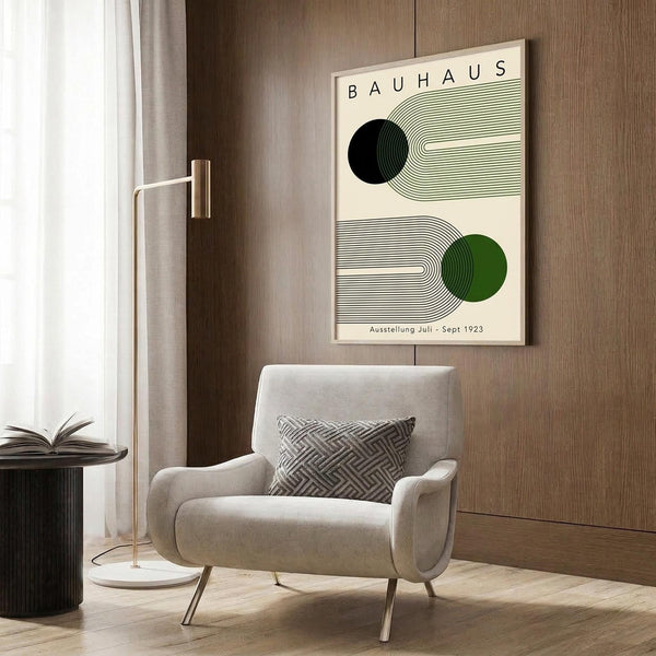 May include: Vintage-style Bauhaus poster with geometric design featuring black and green circles surrounded by concentric lines on cream background, displayed above modern beige armchair with patterned pillow in contemporary living room with wood paneling, brass floor lamp, and side table