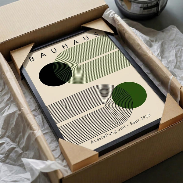 May include: Framed Bauhaus exhibition poster with geometric design featuring curved concentric lines, black and green circles on cream background, displayed in black frame inside cardboard shipping box with protective tissue paper wrapping