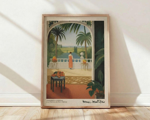 May include: Framed poster print featuring a tropical terrace scene with woman in red dress viewing palm trees and landscape through arched doorway. Vibrant greens, warm oranges, decorative balustrade, fruit on dark table in foreground. Light wood frame displayed on wooden floor against white wall with natural window shadows.