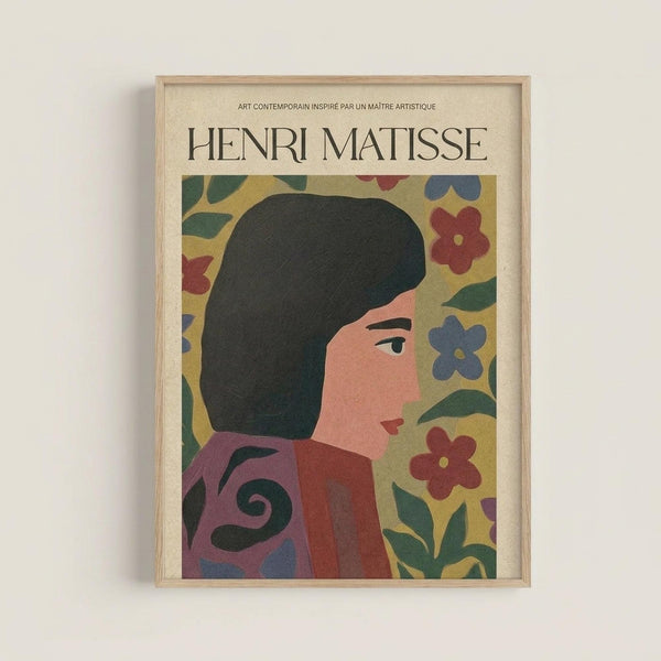 May include: Framed art print featuring a stylized portrait of a woman with dark hair in profile, wearing a red garment with decorative swirls. She's surrounded by colorful flowers in red and blue against a yellow background, rendered in Matisse's characteristic cut-out style. The print has "HENRI MATISSE" text at the top and is displayed in a light wood frame against a white wall.