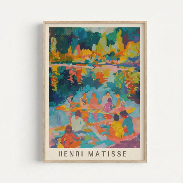 May include: Framed art print featuring a vibrant Fauve-style painting of figures relaxing by a colorful lake or pond, surrounded by brilliant autumn foliage in oranges, yellows, blues and greens. The artwork shows multiple people sitting and lounging in a natural setting with bold, expressive brushstrokes. Artist name "HENRI MATISSE" appears in gray text below the image. Light wood frame hangs on white wall.