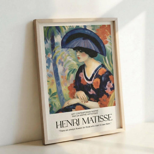 May include: Framed art print leaning against white wall showing colorful Fauve-style painting of woman in blue hat and floral dress beneath palm fronds, with Henri Matisse attribution text below artwork in natural wood frame