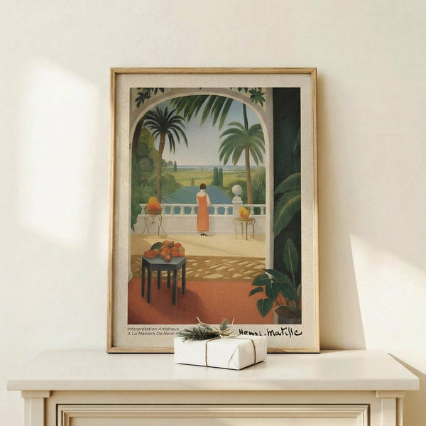 May include: Framed art print in natural wood frame showing tropical terrace scene with figure in orange dress on white balustrade, palm trees, small table with oranges, and Mediterranean landscape beyond archway. White wrapped gift with twine sits on light wood console table against cream wall.