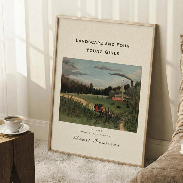 May include: A framed art print leaning against a white wall on a textured cream rug, showing Henri Rousseau's pastoral landscape painting with four young girls in a grassy meadow, trees, and industrial chimney smoke. A white coffee cup sits on a wooden block nearby, with soft natural lighting creating gentle shadows.