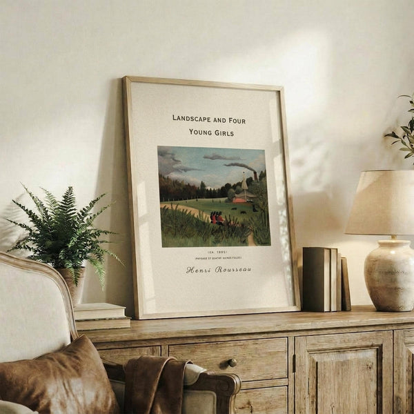 May include: Framed vintage art print of pastoral landscape with rolling green hills, trees, and small red figures in foreground, displayed on rustic wooden sideboard beside fern plant, books, ceramic vase, and beige armchair in warm-toned living room setting