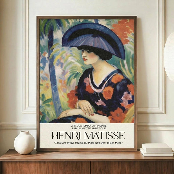 May include: Framed poster featuring a woman in a blue wide-brimmed hat and floral dress in vibrant Fauvism style with bold brushstrokes and tropical colors. The artwork shows French text and an inspirational quote at the bottom. The frame sits on a wooden console beside a white ceramic vase and stacked books against cream wainscoting walls in a bright interior setting.