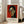 May include: Framed poster print featuring an abstract portrait of a woman with long black hair, geometric facial features in green and orange tones against a red background, attributed to Henri Matisse with French text and quote about flowers below the artwork, displayed on hardwood floor next to beige upholstered chair in bright room with white walls and windows