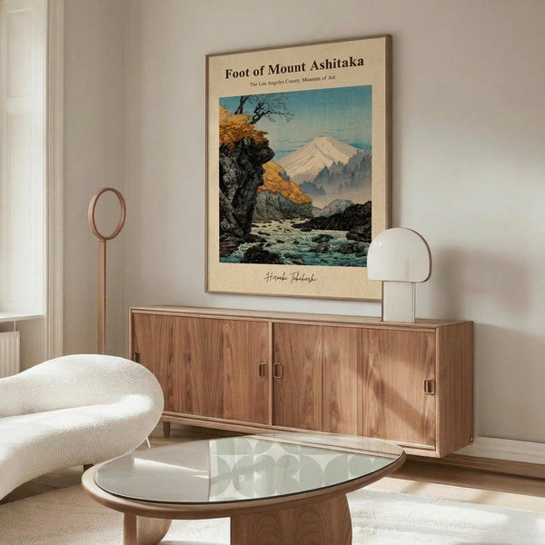 May include: Japanese woodblock print poster showing Mount Fuji landscape with autumn trees and rocky stream, displayed above walnut credenza in modern living room with white curved chair, glass coffee table, and warm lighting creating shadows on beige walls.