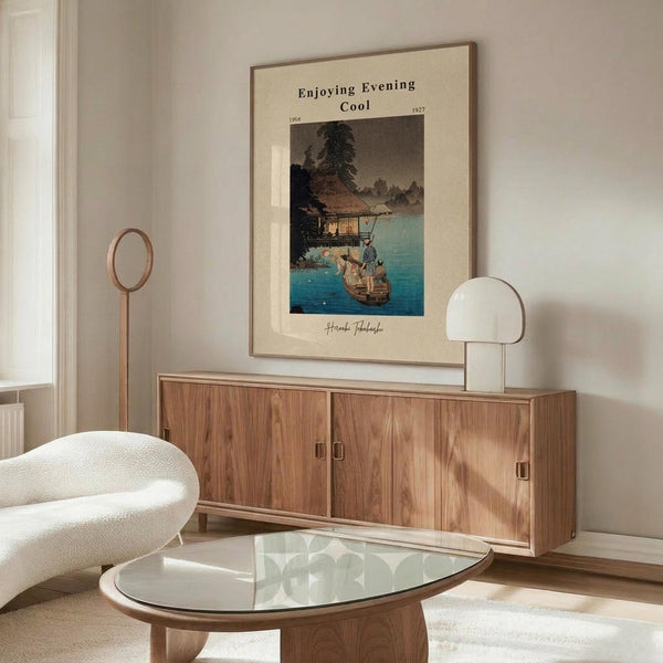 May include: Japanese woodblock-style poster print hanging above wooden sideboard in modern living room. Artwork shows lakeside scene with traditional house, boats, and evening sky in blues and earth tones. Room features cream chair, glass coffee table, white table lamp, and wooden floor lamp. Neutral walls and natural lighting create serene atmosphere.