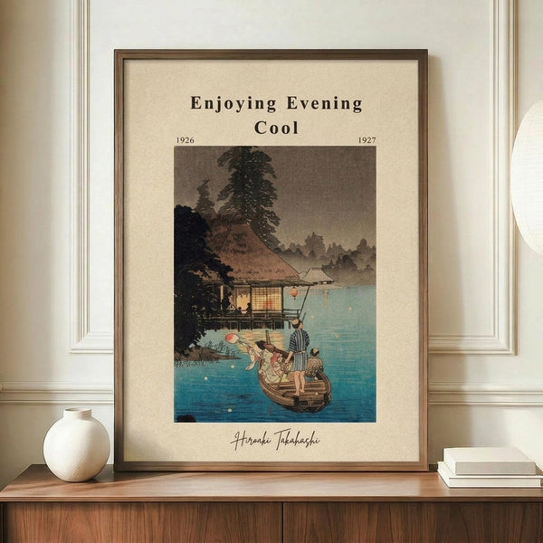 May include: Framed Japanese woodblock print showing people in a small boat on blue water near a traditional house with thatched roof and large tree at dusk. Print has cream matting in brown wooden frame, displayed on walnut credenza beside white ceramic vase and stacked books against white paneled wall.