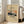 May include: Framed vintage-style poster featuring Mount Fuji with snow-capped peak against orange sunset sky, silhouetted trees in foreground, cream background with black text reading "Katsuyama Neighborhood" and "The Los Angeles County Museum of Art" and artist name, displayed in light wood frame leaning against white wall next to beige upholstered chair in bright living room with large windows.