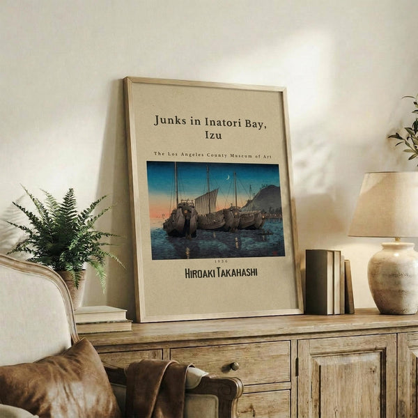May include: Framed vintage-style poster featuring traditional Japanese sailing vessels on water at twilight, displayed on rustic wooden sideboard alongside fern plant, ceramic vase, lamp, and books in neutral-toned living room setting