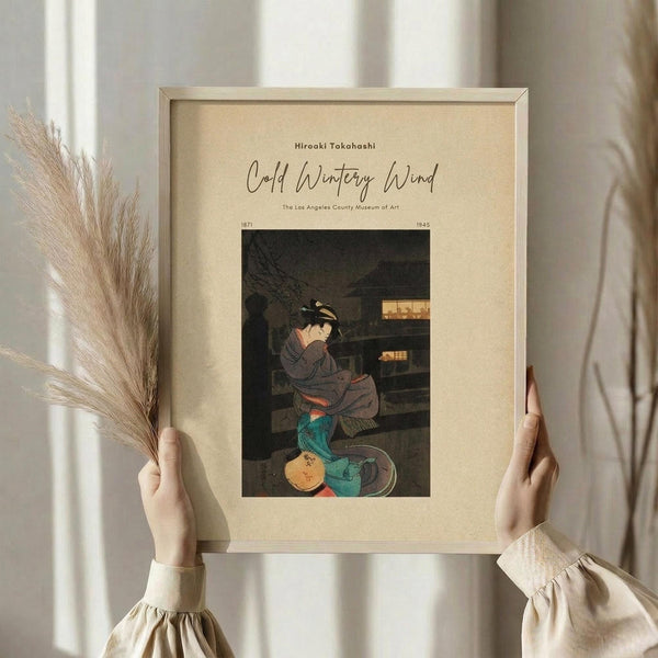 May include: Hands holding a framed vintage Japanese woodblock print showing a woman in traditional dress kneeling beside colorful ceramic vessels. The artwork features muted earth tones against a dark background. Light wooden frame on cream matting. Person wearing beige ruffled sleeves holds dried pampas grass in one hand while displaying the museum-style art print near white curtained window.