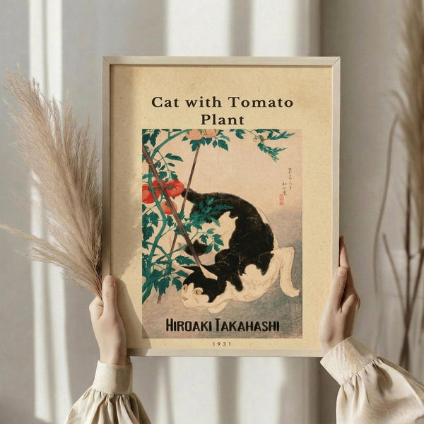 May include: Hands holding a framed vintage Japanese woodblock print showing a black and white cat sitting beside a tomato plant with red tomatoes and green leaves. The artwork has aged beige paper background with Japanese text and "Cat with Tomato Plant" and "Hiroaki Takahashi 1931" printed below. Person wears cream ruffled sleeves and holds dried wheat stems, standing against white curtained window.