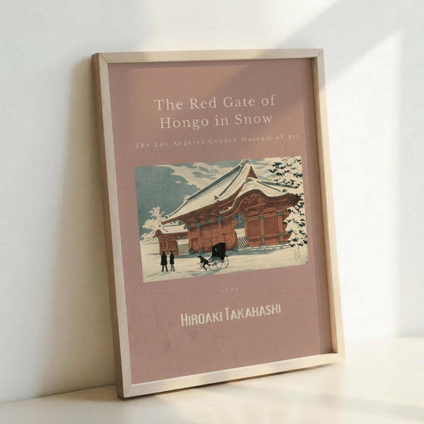 May include: Framed art print leaning against white wall showing Japanese woodblock-style illustration of traditional red temple building in snow with small figures and cart in foreground. Print has dusty rose background with cream text reading "The Red Gate of Hongo in Snow" and "Hiroaki Takahashi" with "1926" date. Light wood frame, positioned at angle showing depth and shadow on wall.