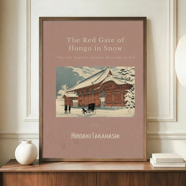 May include: Framed vintage Japanese woodblock print poster displayed on wooden sideboard beside white ceramic vase and books. The artwork shows a traditional red temple building covered in snow with small figures and cart in courtyard. Dusty rose background with cream text identifying the Los Angeles County Museum of Art and artist Hiroaki Takahashi, dated 1926. Thin dark wood frame against cream wainscoted wall.