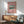 May include: Framed vintage Japanese woodblock print of snow-capped Mt. Fuji with lake and trees on pink background, displayed above modern wood sideboard with white ceramic lamp in minimalist room with mint green mid-century armchair and natural lighting casting geometric shadows on white wall.
