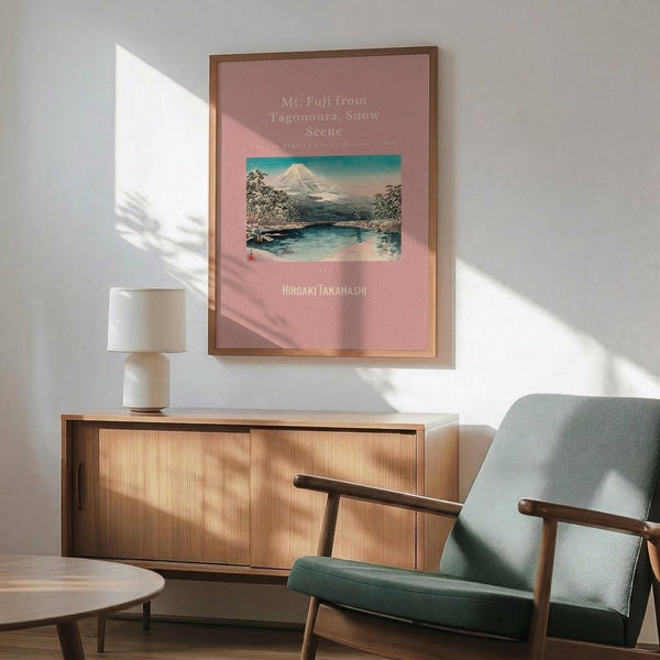 May include: Framed vintage Japanese woodblock print of snow-capped Mt. Fuji with lake and trees on pink background, displayed above modern wood sideboard with white ceramic lamp in minimalist room with mint green mid-century armchair and natural lighting casting geometric shadows on white wall.