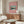 May include: Framed pink poster featuring Japanese woodblock print of snow-capped Mt. Fuji reflected in blue water, displayed above walnut credenza in modern living room with white curved chair, glass coffee table, and brass floor lamp