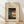 May include: Framed vintage Japanese woodblock print showing blue bellflowers and foliage beside a red paper lantern with two black silhouetted figures beneath it, displayed in light wood frame against white wall on wooden floor with natural window lighting.