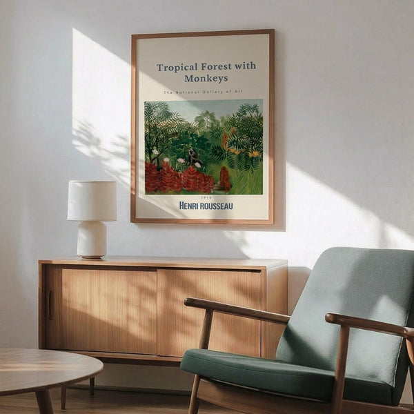 May include: Framed Henri Rousseau tropical forest poster print hanging above a wooden sideboard in a bright living room. The artwork shows dense green jungle foliage with red flowering plants and monkeys. Museum-style poster has cream background with brown wooden frame. Mid-century modern furniture includes sage green upholstered chair with wood arms and white ceramic table lamp. Natural sunlight casts shadows across white wall.