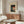 May include: Framed Japanese woodblock print featuring bellflowers and a red lantern displayed above a walnut credenza in a minimalist living room. The artwork shows dark silhouettes against cream matting in a thin wood frame. Modern white sculptural chair and glass oval coffee table complete the serene, neutral-toned space with natural lighting.