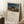 May include: Framed art print leaning against white wall showing Henri Rousseau's famous painting of a sleeping figure in striped robes beside a lion under moonlight in desert landscape. Light wood frame, cream matting with black text below artwork. Cozy room setting with white coffee cup on wooden block, cream throw blanket, and soft natural lighting creating shadows on textured rug.