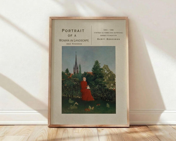May include: Framed art print leaning against white wall on light wood floor. Print shows woman in red dress sitting in lush green landscape with church spire in background. Cream matting surrounds colorful naive-style painting in thin wooden frame. Soft natural lighting creates diagonal shadows across white textured wall.