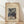 May include: Framed vintage Japanese woodblock print poster featuring snow-covered cedar trees with small figures walking along a snowy mountain path. The artwork shows tall brown tree trunks with white snow-laden branches against a blue winter sky. The cream-colored poster has black text at the top identifying the artist and artwork details. The natural wood frame sits on light wooden flooring against a white wall with soft natural lighting casting gentle shadows.