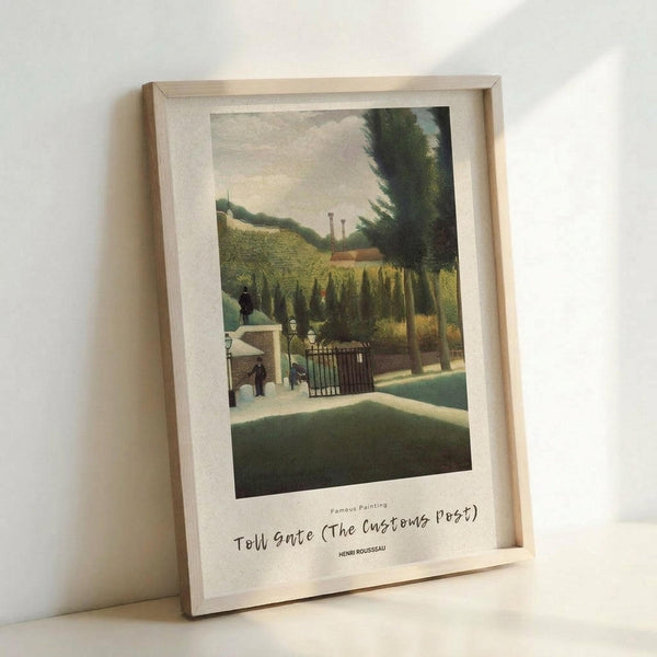 May include: Framed art print of a naive-style painting showing a Parisian street scene with toll gate, featuring small figures near a white customs building, lush green trees and hills in background, industrial smokestacks in distance. Print has white border with handwritten-style text identifying the artwork and artist Henri Rousseau. Light wooden frame leans against white wall.