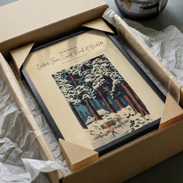 May include: Framed vintage Japanese woodblock print showing tall cedar trees with detailed bark and foliage against a cloudy sky, with small figures walking on a path below. The artwork features earth tones of brown, green, and cream in traditional ukiyo-e style. Black frame sits in opened cardboard shipping box with white tissue paper padding on wooden surface.