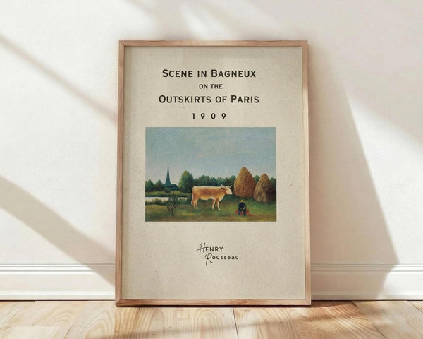 May include: Framed vintage art poster featuring Henri Rousseau's pastoral painting of a cow grazing in a green field with large haystacks, trees, and church spire in background. Cream-colored poster with black text reading "Scene in Bagneux on the Outskirts of Paris 1909" and artist signature. Natural wood frame leaning against white wall on light wooden floor with soft shadows.