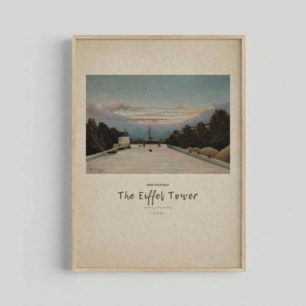 May include: Framed art print hanging on white wall showing Henri Rousseau's 1898 painting of the Eiffel Tower viewed from the Seine River at dusk, with pale blue-green sky, pink clouds, dark trees lining the riverbanks, and small boats on the water. Light wood frame with cream matting and black text below the image.