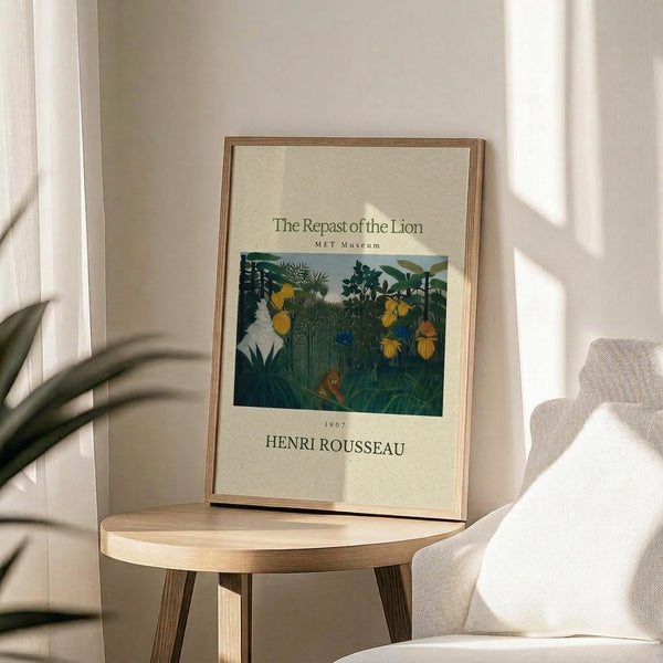 May include: Framed museum poster featuring Henri Rousseau's jungle painting with a lion among lush green foliage and yellow fruit, displayed on a round wooden side table next to a beige upholstered chair. Soft natural lighting creates gentle shadows across the neutral-toned room setting with a plant visible in the corner.